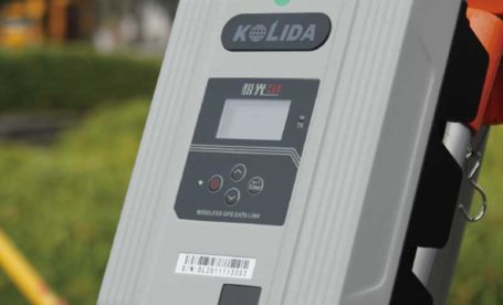Kolida wireless GPS data link device mounted on a tripod in a field survey environment, used for transmitting RTK correction signals during GNSS operations.
